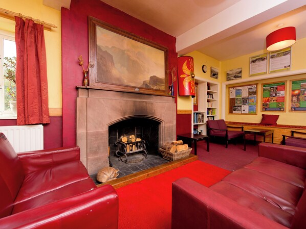 Una habitación acogedora con chimenea, asientos de cuero rojo y una estantería con carteles informativos.