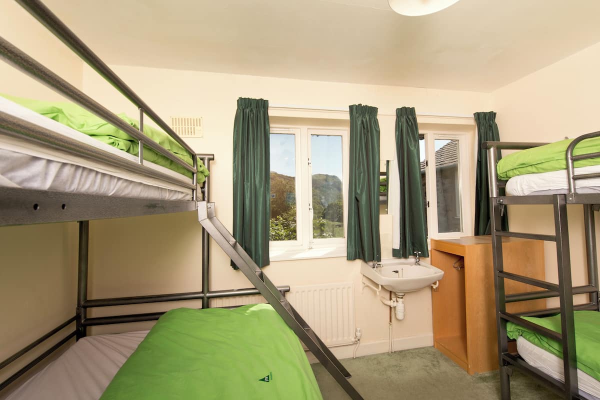 A bunk room with two bunk beds, a window with curtains, a sink, and a radiator.