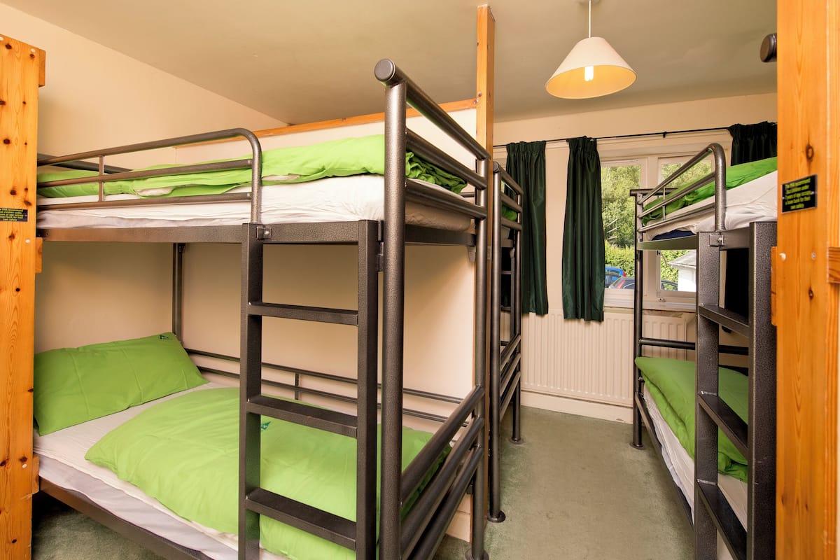 A bunk bed room with green bedding, a wooden door, and a window with curtains.
