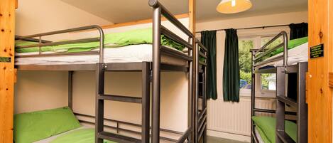 Habitación con literas, ropa de cama verde, una puerta de madera y una ventana con cortinas.