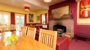 Un comedor con una mesa de madera, sillas, una chimenea y una pared roja decorativa.