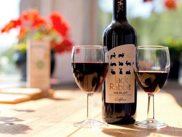 A bottle of Jack Rabbit Merlot wine and two glasses on a wooden table.