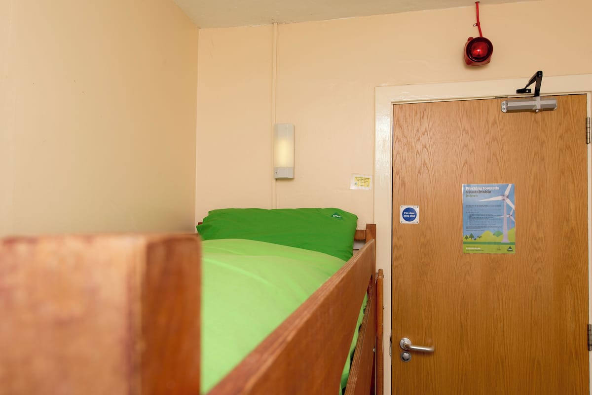 A room with a wooden bunk bed, a wooden door with a sign, and a red hanging object.