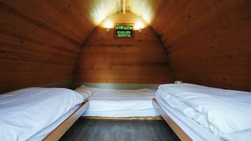 Una habitación pequeña y acogedora con paredes de madera y techo inclinado. Hay dos camas individuales con ropa blanca y una ventana pequeña al fondo de la habitación.