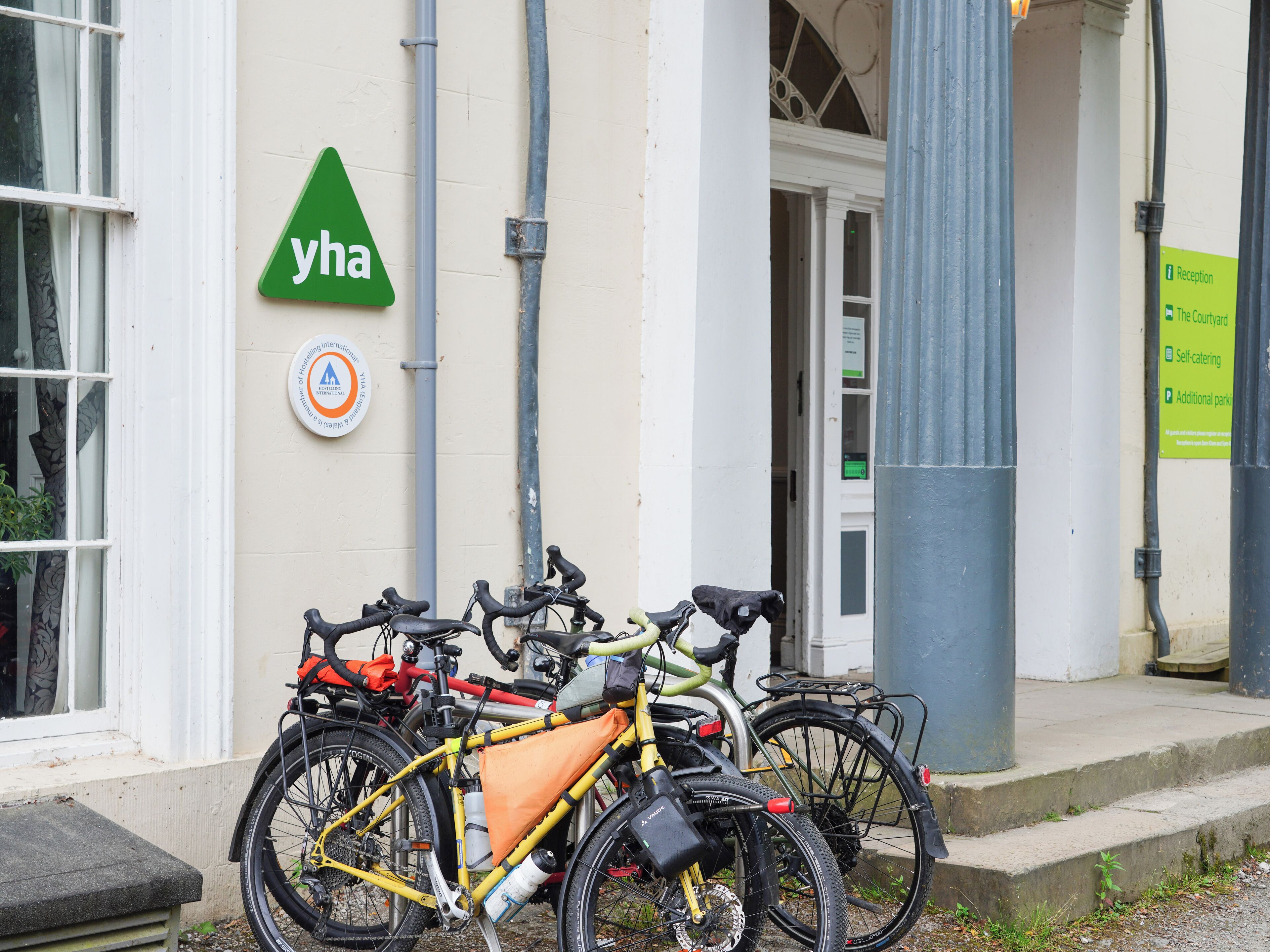 Un edificio con un cartel que dice "yha" y una señal de recepción. Hay bicicletas estacionadas afuera.