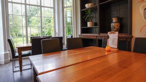 A dining area with a wooden table, chairs, and a menu stand. Large windows provide a view of greenery outside. - YHA Hawkshead - Hostel (Ambleside)