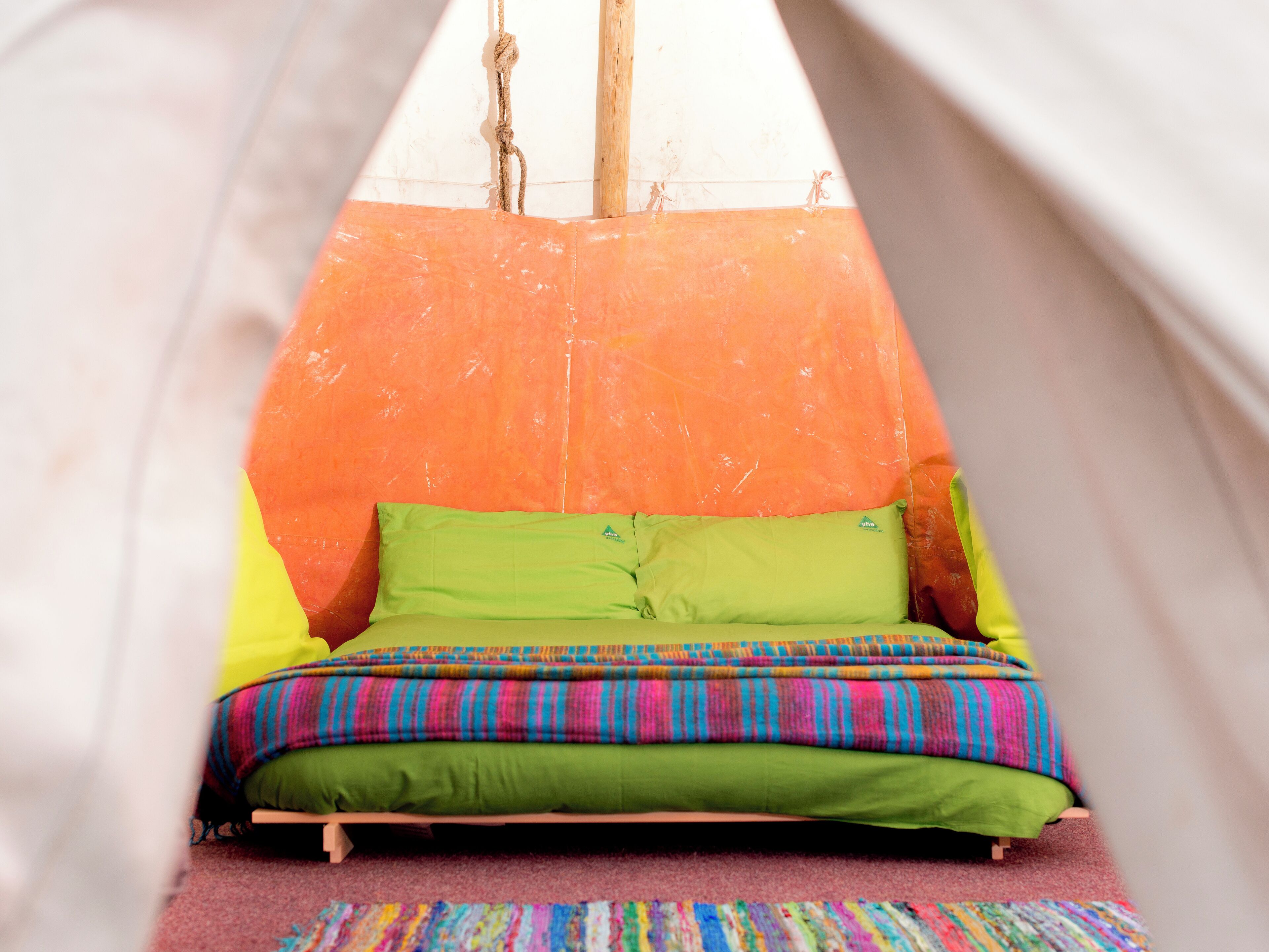 A bed with colorful bedding, a striped rug, and a tent-like structure with a rope and wooden poles.