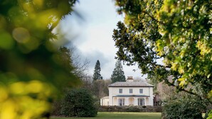 A large, white building with a symmetrical facade, surrounded by a well-maintained lawn and dense greenery. - YHA Hawkshead - Hostel (Ambleside)