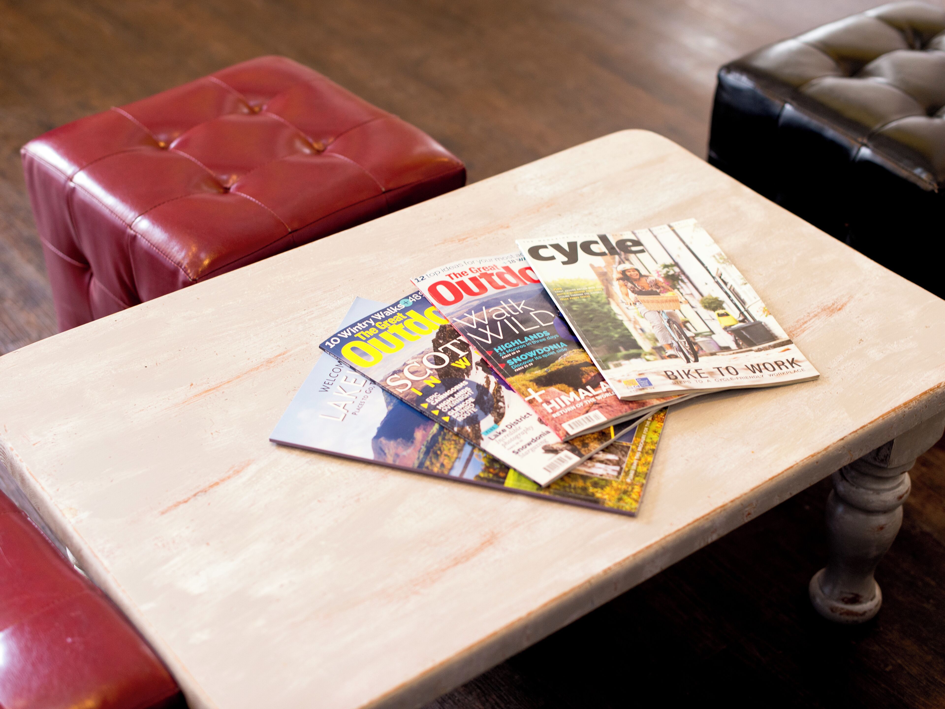 Una mesa de madera con revistas y un otoman de cuero rojo.