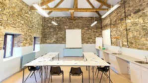 A conference room with a long table, black chairs, a whiteboard, stone walls, and a kitchen area with a sink. - YHA Hawkshead - Hostel (Ambleside)