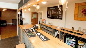 Un espace bar avec un comptoir en bois, des ampoules suspendues et un tableau affichant le menu.