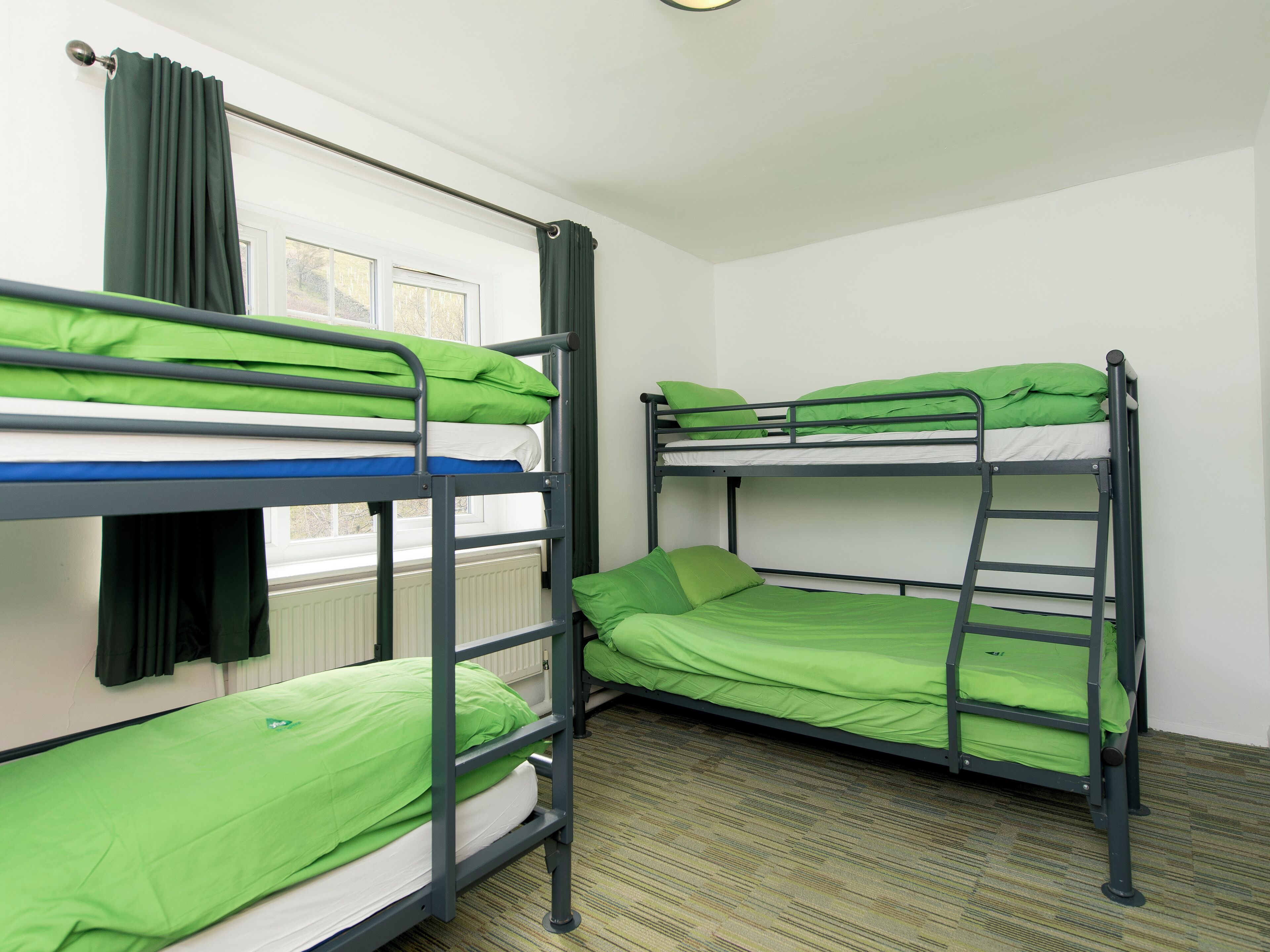 Une chambre avec des lits superposés, une fenêtre avec des rideaux et un radiateur.