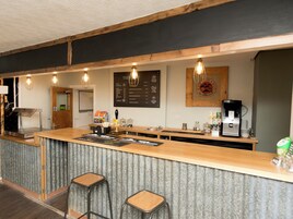 Uma área de bar com balcão de madeira, banquetas, máquina de café e um quadro de cardápio.