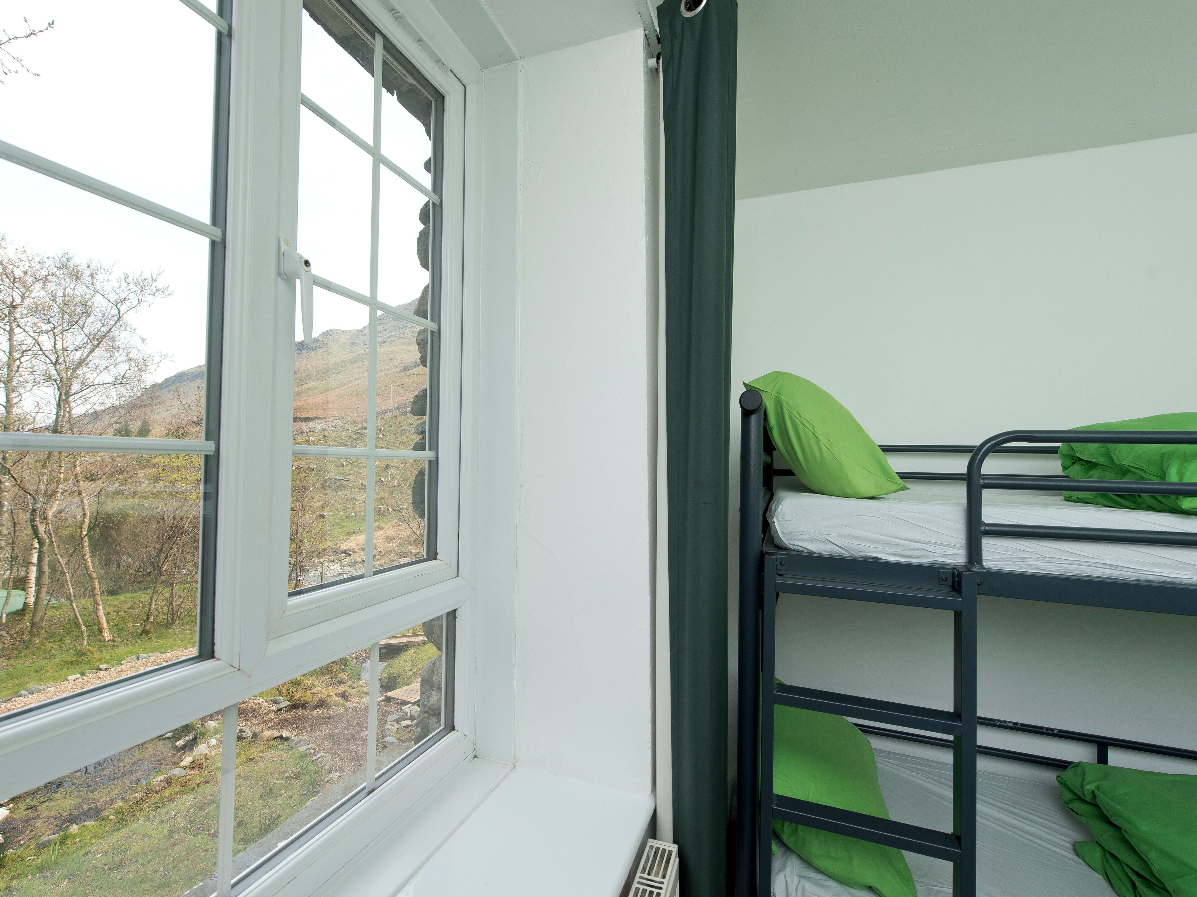 A bunk bed with green pillows, a window with a view of a mountainous landscape, and a white wall.