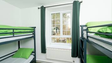 A dormitory room with bunk beds, a window with curtains, and a radiator.