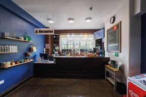 A reception area with a blue wall, a reception desk, a chalkboard menu, and a clock on the wall. - YHA Ilam Hall - Hostel (Ashbourne)