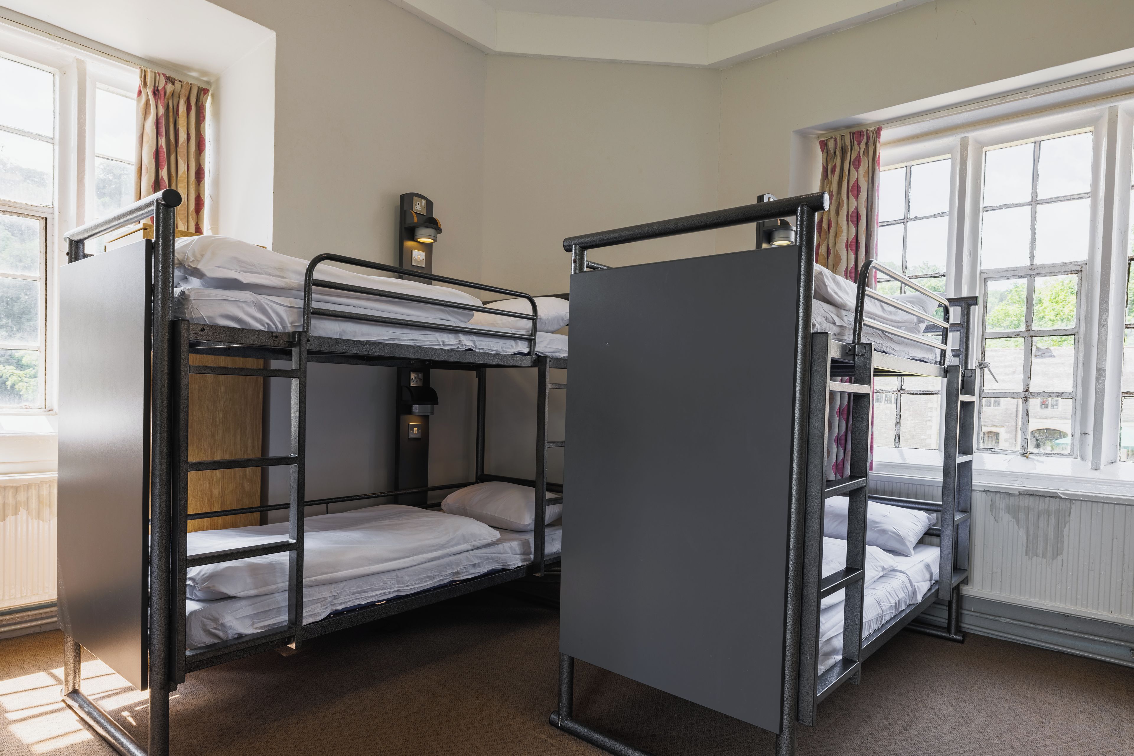 A bunk bed room with a window, a radiator, and a wall-mounted light fixture.