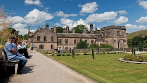 A historic stone building with multiple chimneys, a well-maintained lawn, and a gravel path. - YHA Ilam Hall - Hostel (Ashbourne)