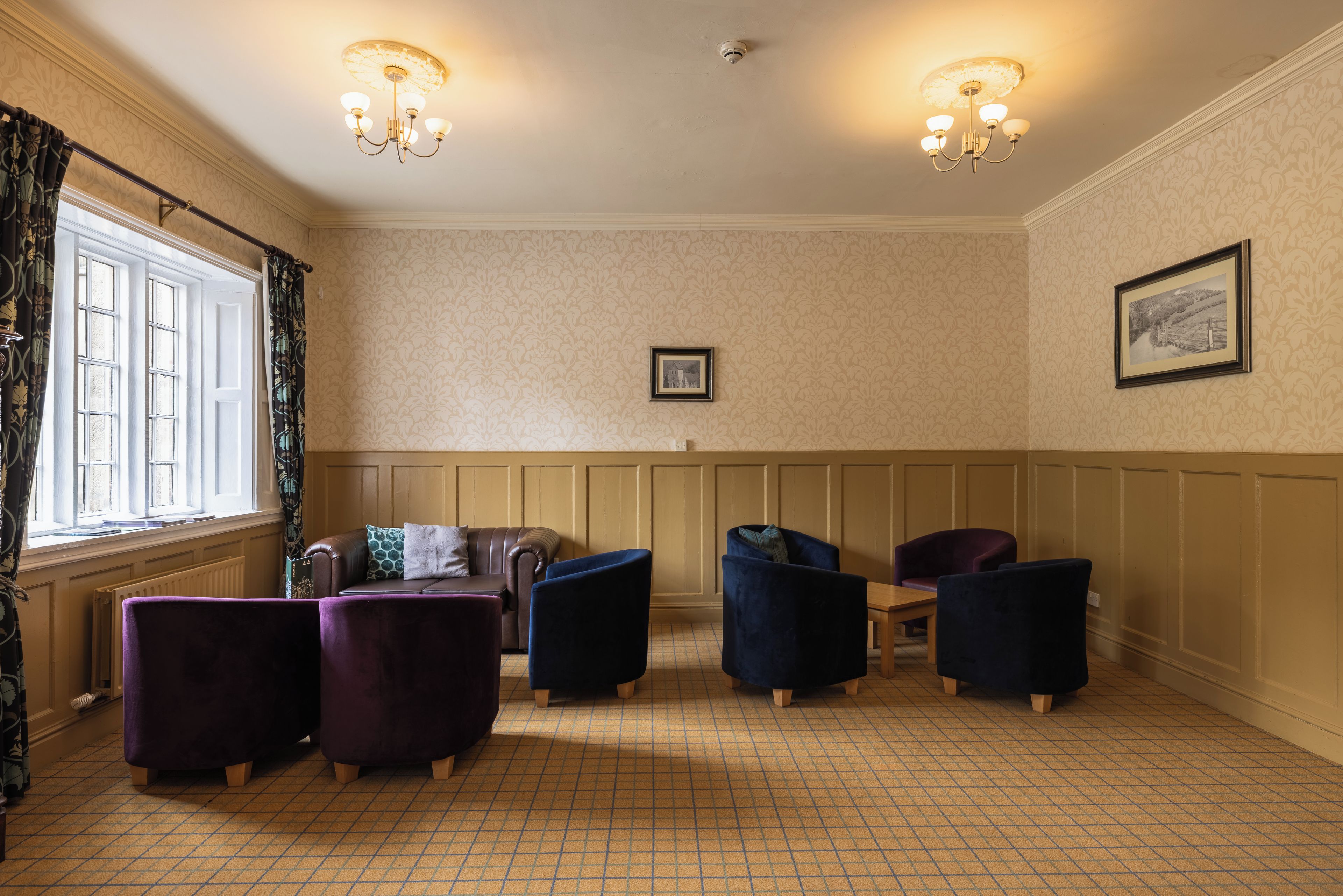 A room with a patterned floor, a brown leather sofa, two armchairs, a wooden table, and a framed picture on the wall.