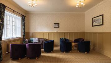 A room with a patterned floor, a brown leather sofa, two armchairs, a wooden table, and a framed picture on the wall.