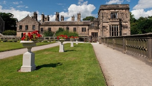 A historic stone building with a symmetrical facade, large windows, and a well-maintained garden with flower beds and a gravel pathway. - YHA Ilam Hall - Hostel (Ashbourne)