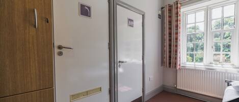 Una habitación con un armario de madera, una puerta con el letrero de baño, un radiador y una ventana con cortinas.