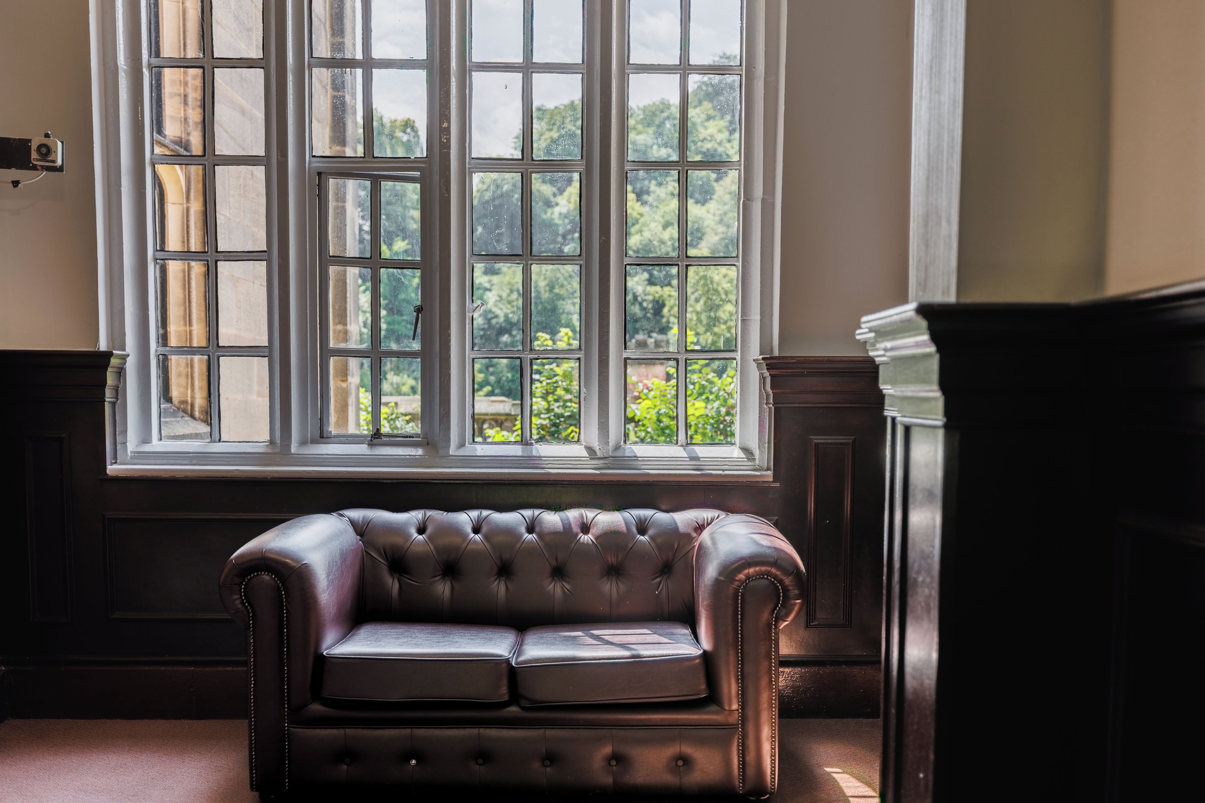 Ein Zimmer mit einem großen Fenster, einem dunkelbraunen Ledersofa und einem Holzschrank.