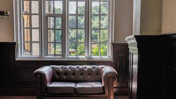 Ein Zimmer mit einem großen Fenster, einem dunkelbraunen Ledersofa und einem Holzschrank.