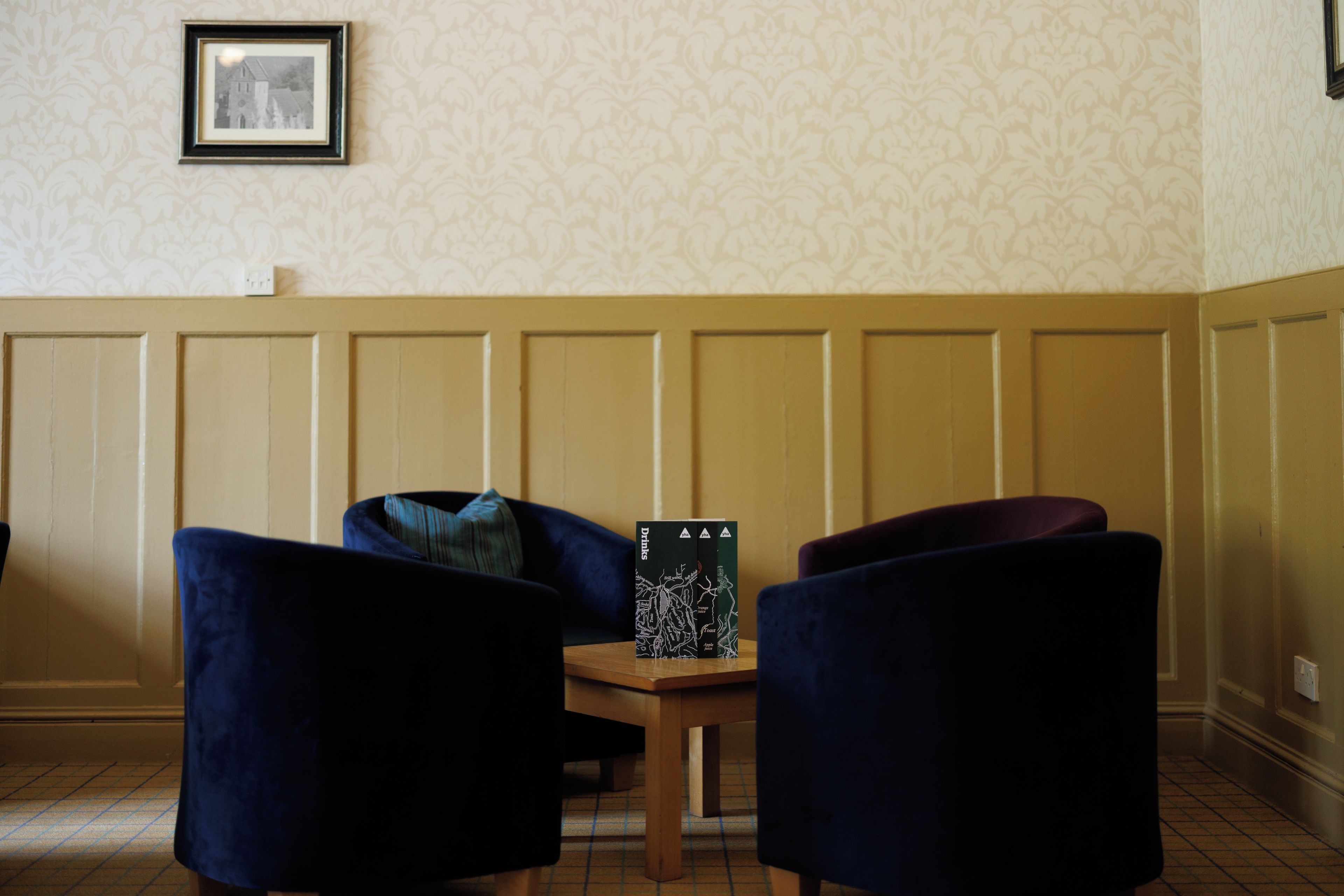 A room with two dark blue chairs, a small wooden table, and a framed picture on the wall.
