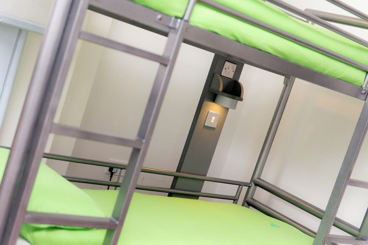 A bunk bed with green bedding and a wall-mounted electrical outlet.