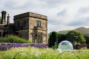 A historic stone building with multiple windows and a garden with purple flowers. - YHA Ilam Hall - Hostel (Ashbourne)