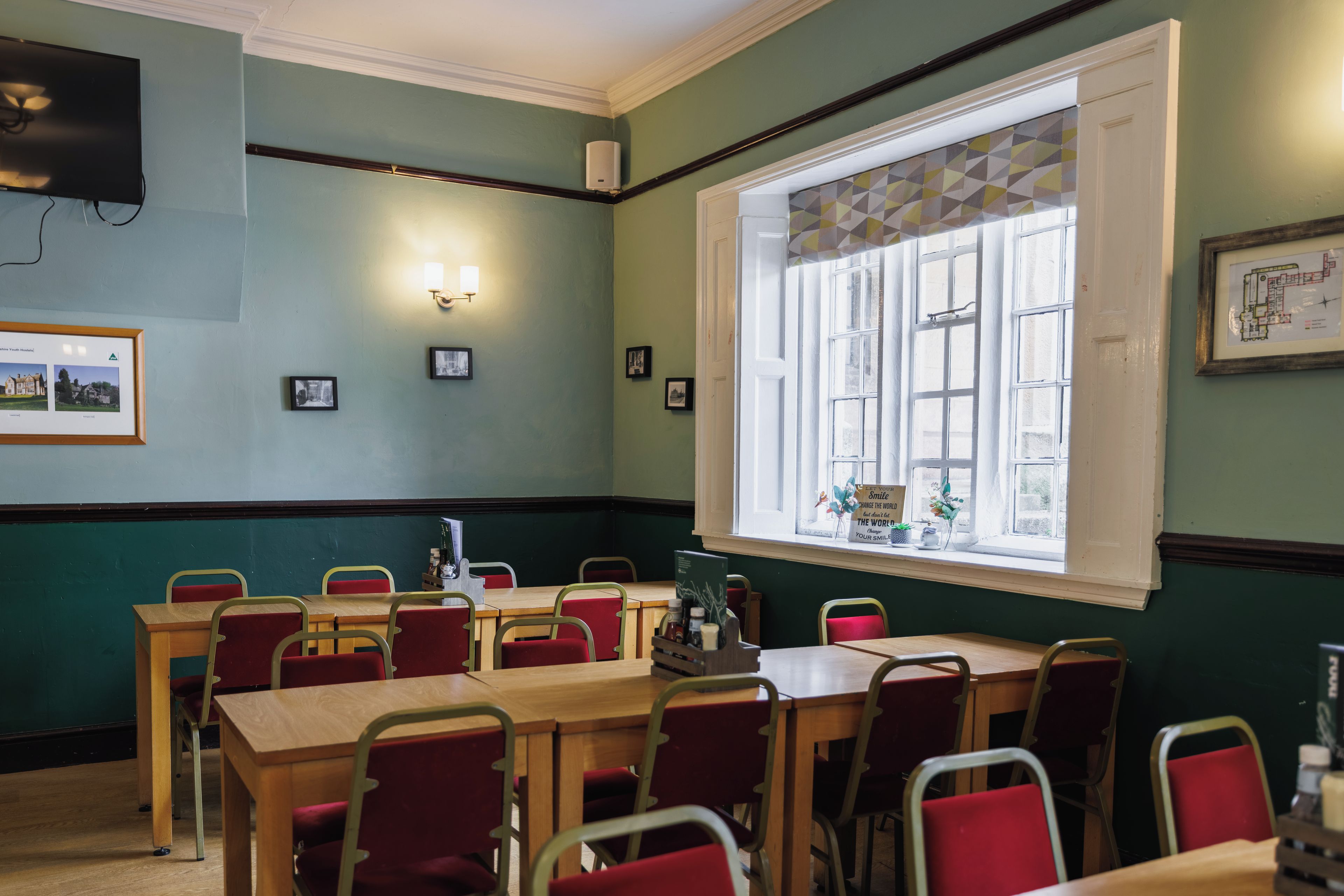 A dining area with tables and chairs, a large window with a view, and wall-mounted lights.