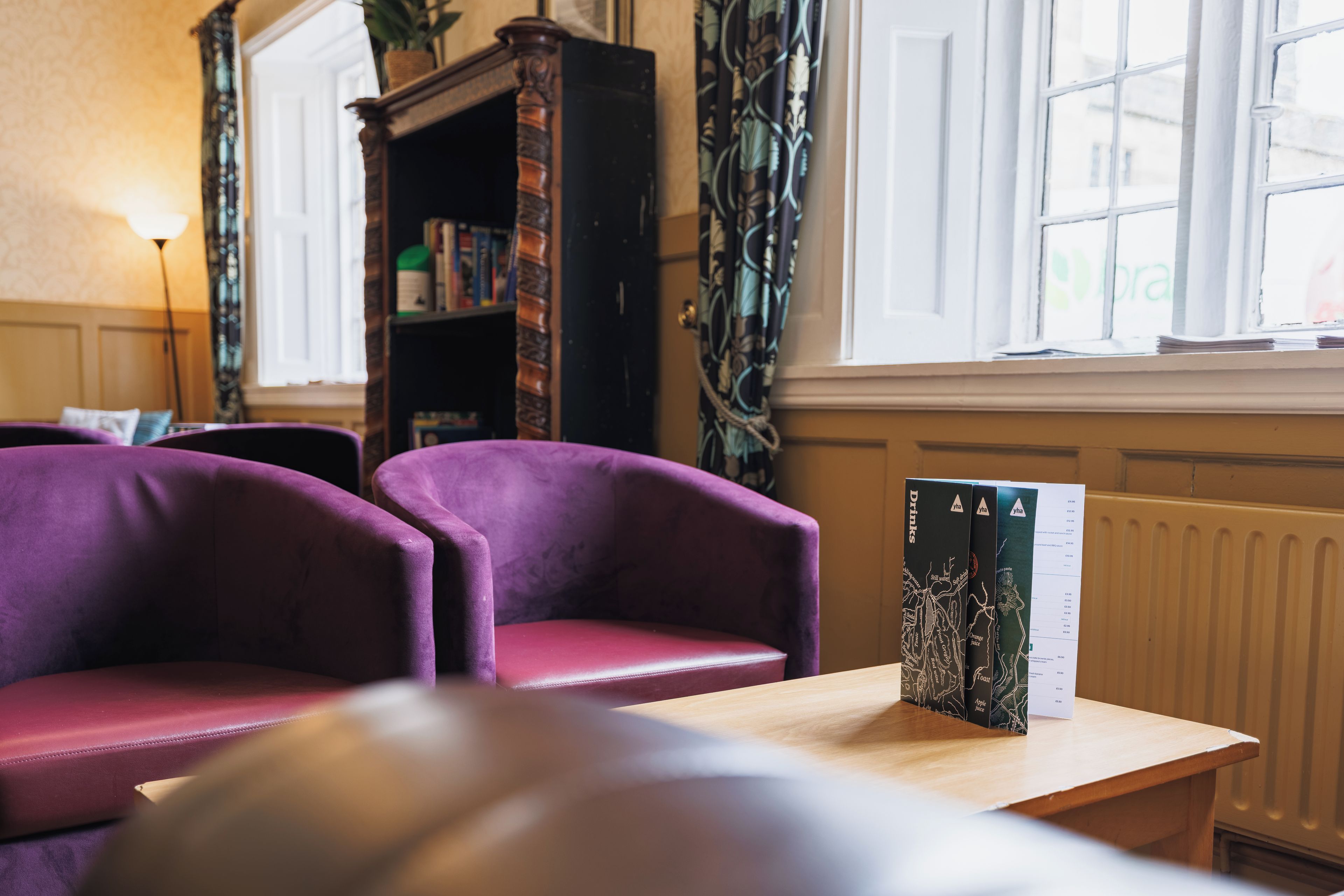 A room with two purple armchairs, a wooden table with a menu, and a bookshelf in the background.