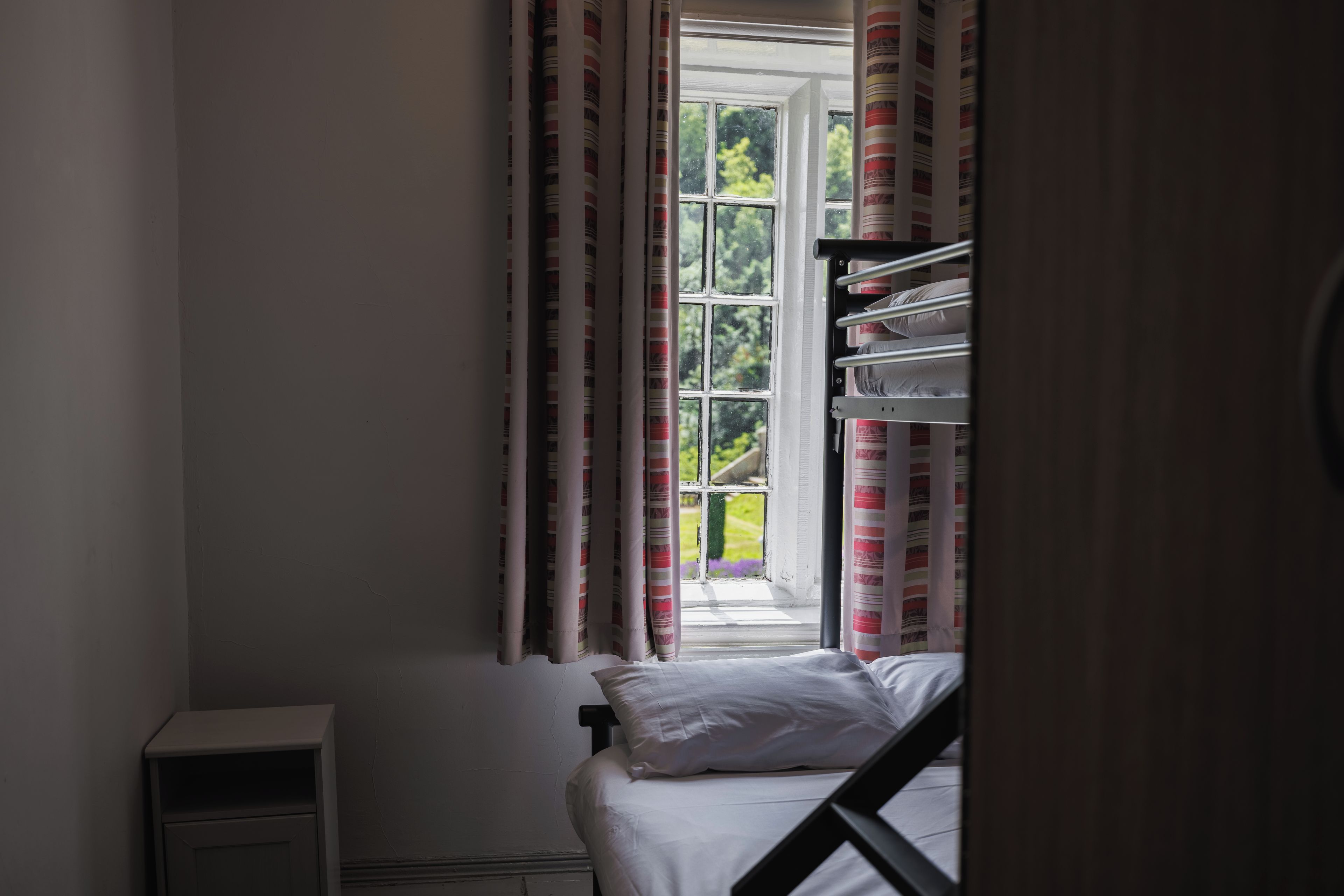 Habitación tipo dormitorio con una cama litera, una mesita de noche pequeña y una ventana con cortinas.