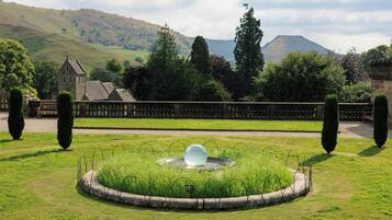 A garden with a spherical water feature, a stone wall, and a distant view of a church and hills.