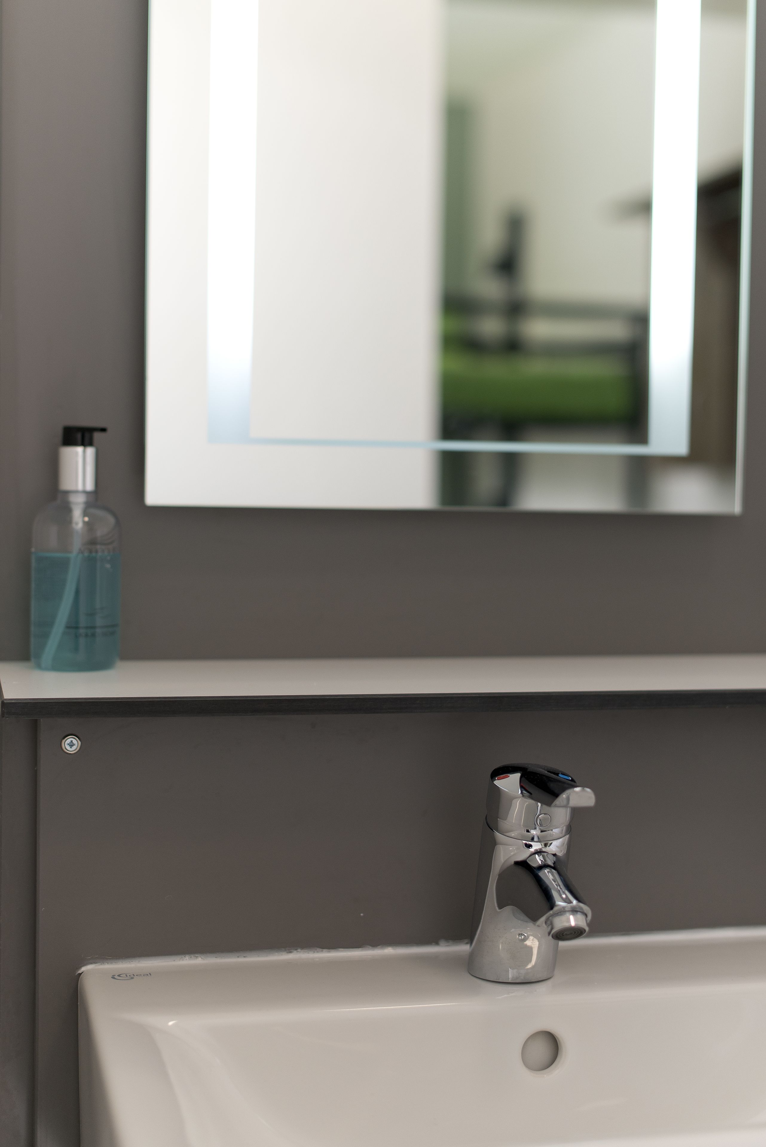 Un baño con un lavamanos blanco, un espejo y una botella de jabón líquido azul sobre la encimera.