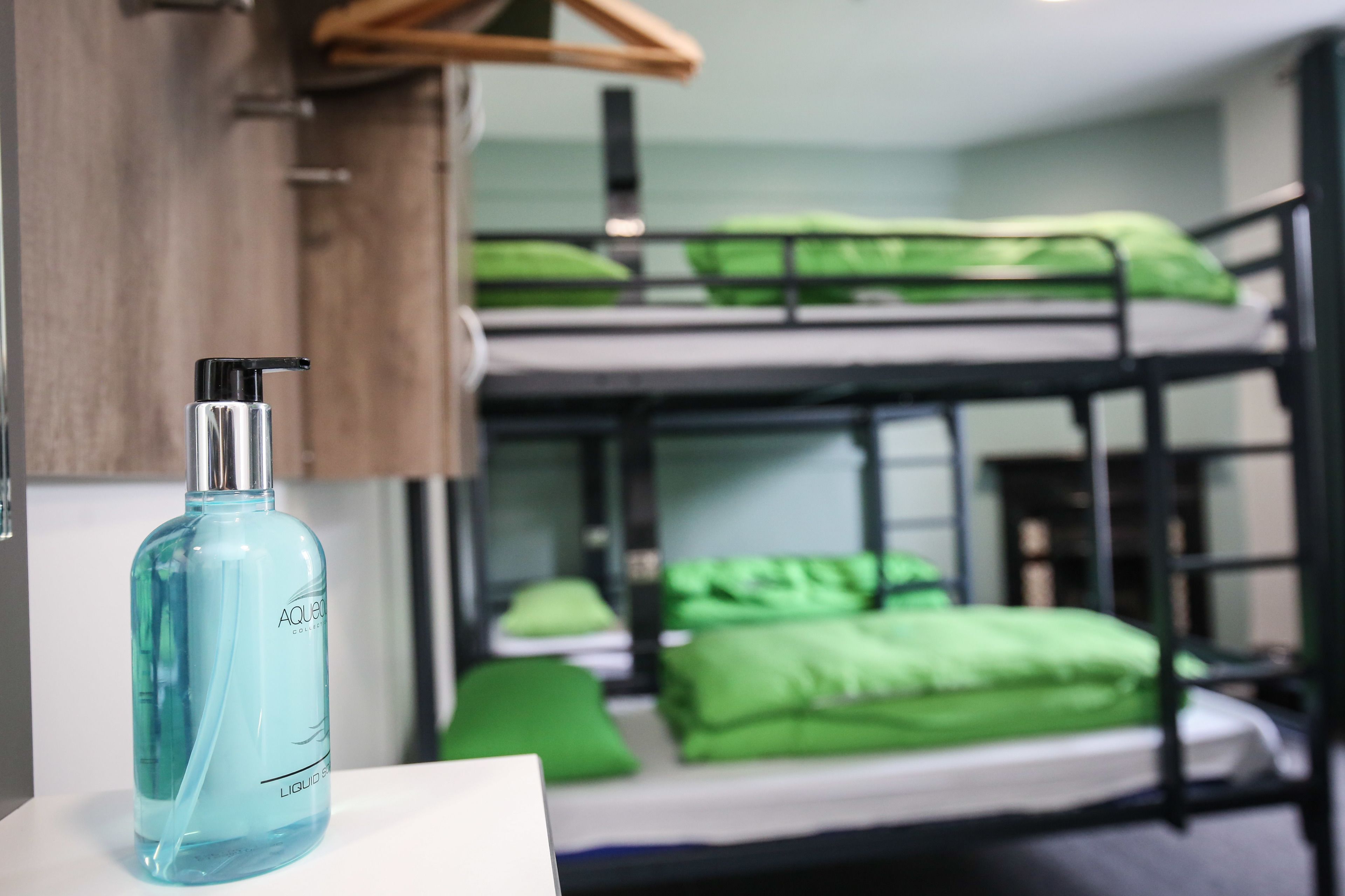 Ein Stockbett mit grüner Bettwäsche, eine Flasche Aquafina Wasser und ein hölzerner Kleiderbügel.