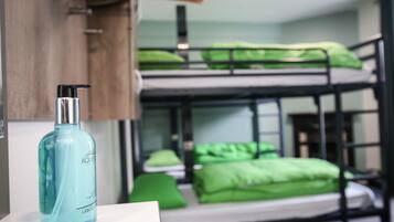 Una cama nido con ropa de cama verde, una botella de Aquafina y un perchero de madera.