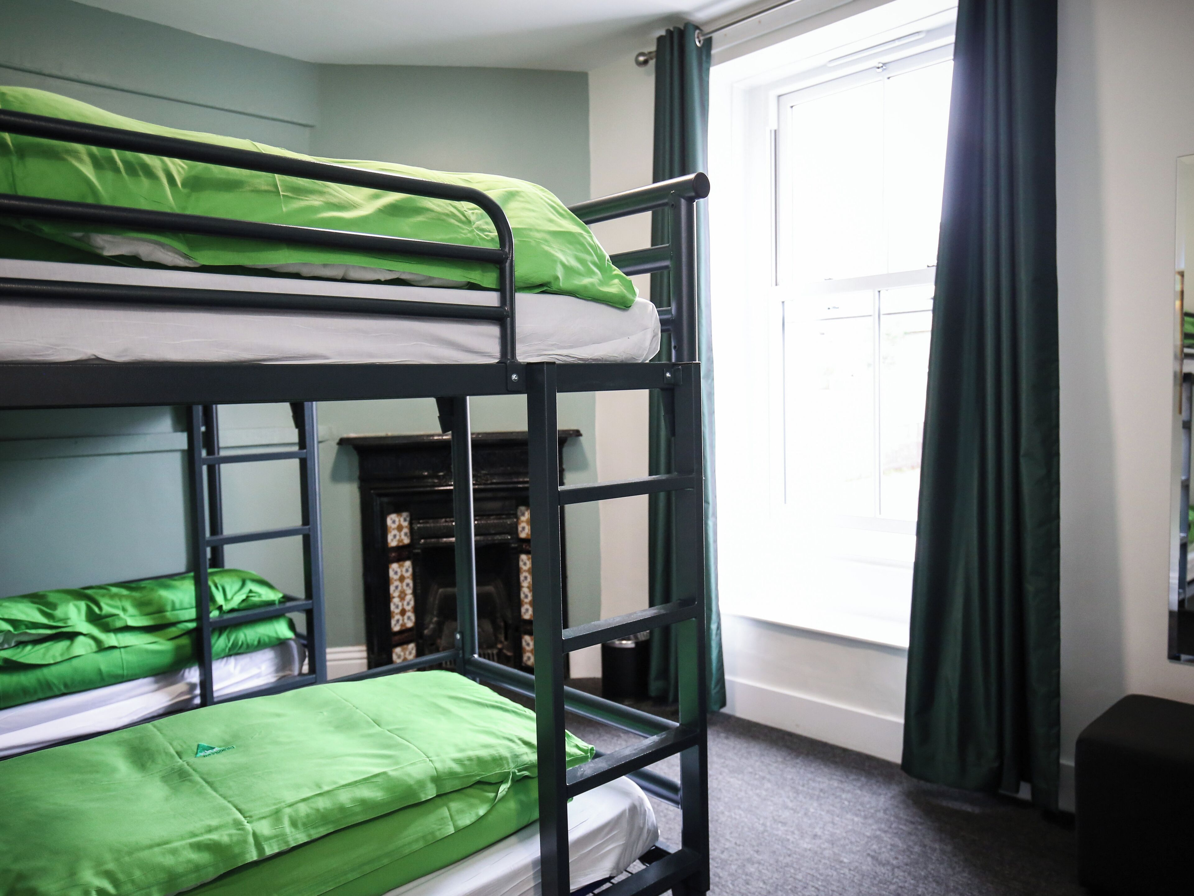 Habitación con literas, ropa de cama verde, chimenea y una ventana con cortinas.