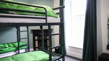 Habitación con literas, ropa de cama verde, chimenea y una ventana con cortinas.