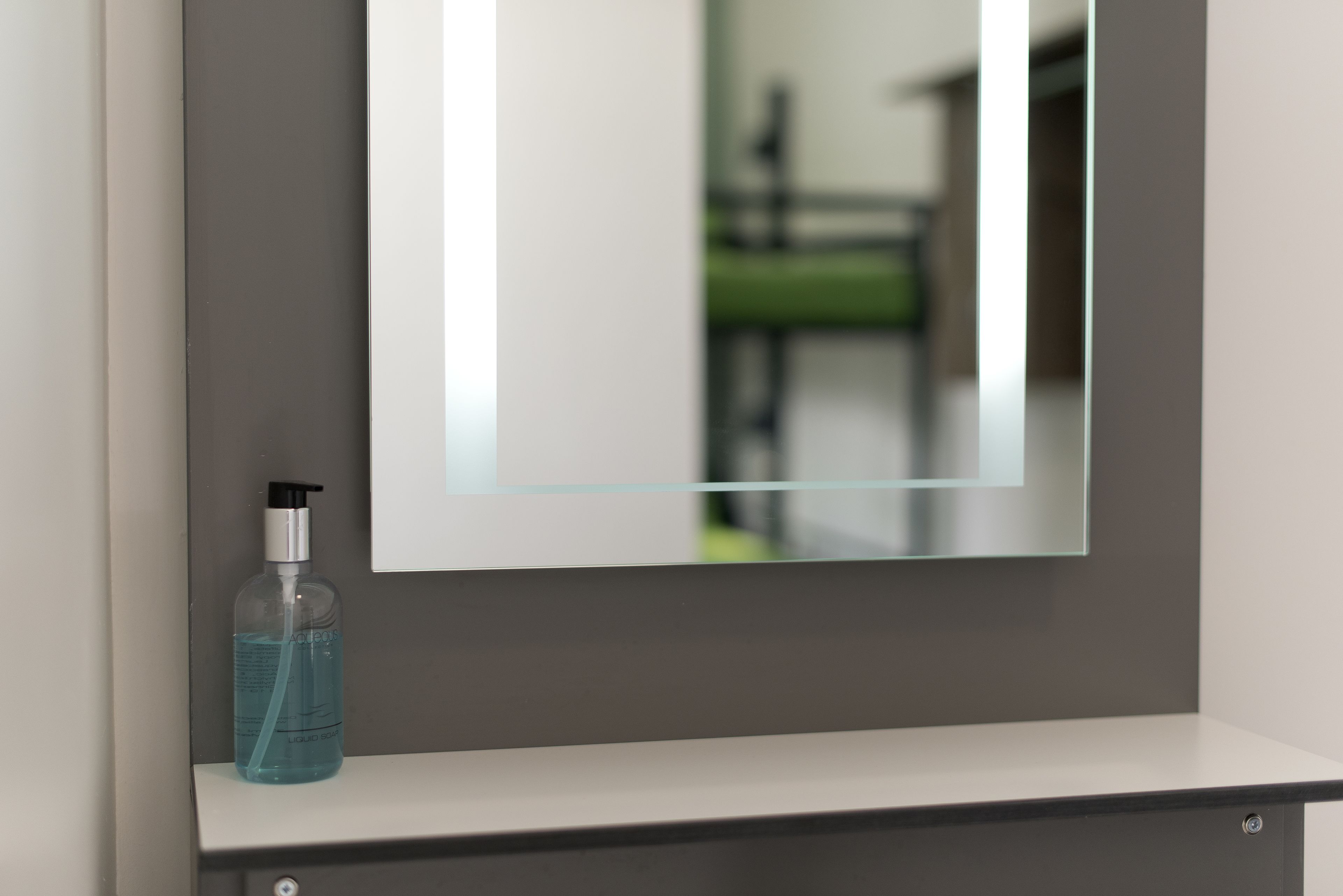 A bathroom with a mirror, a shelf, and a bottle of liquid soap.
