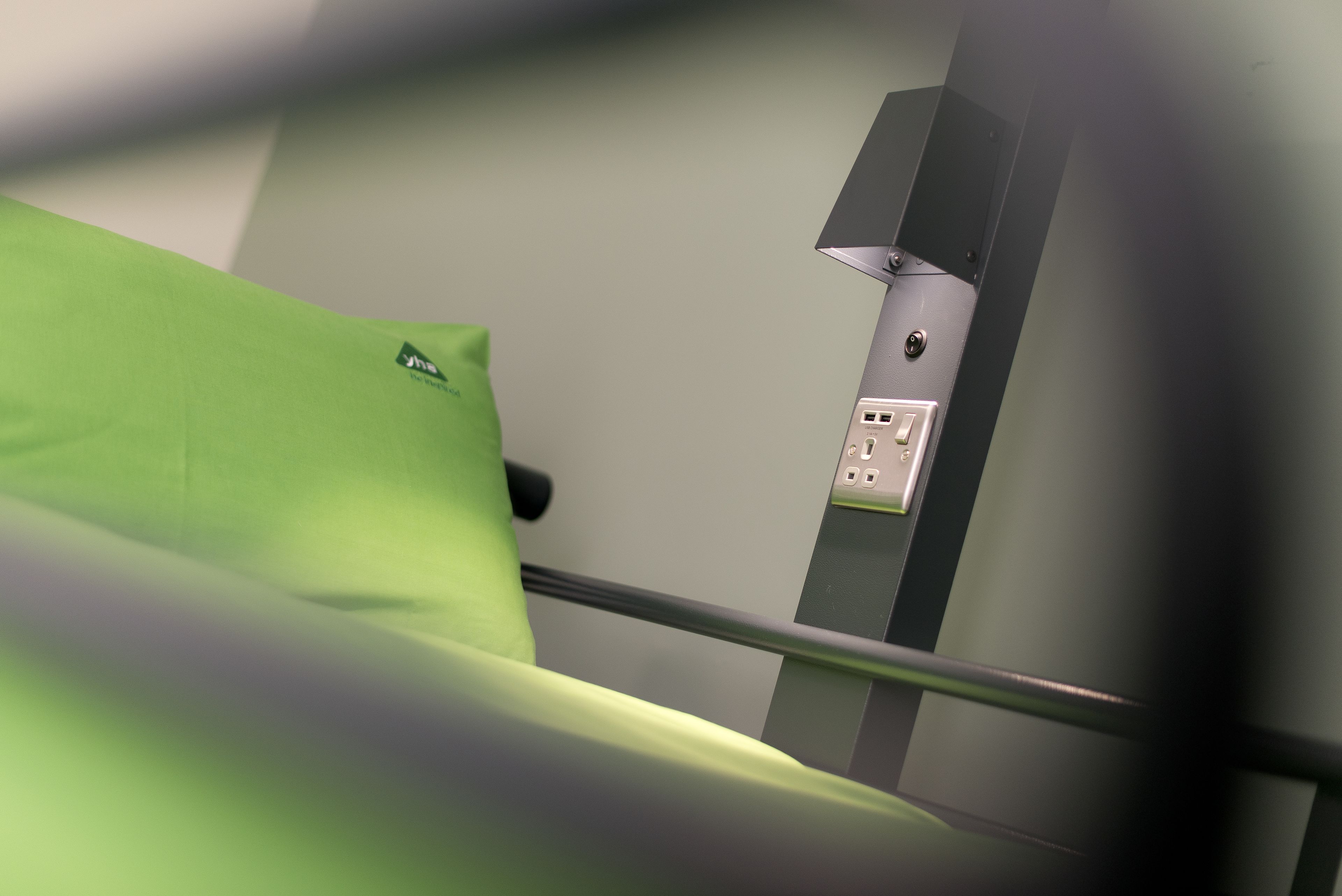 A room with a green bed, a wall-mounted control panel, and a metal railing.