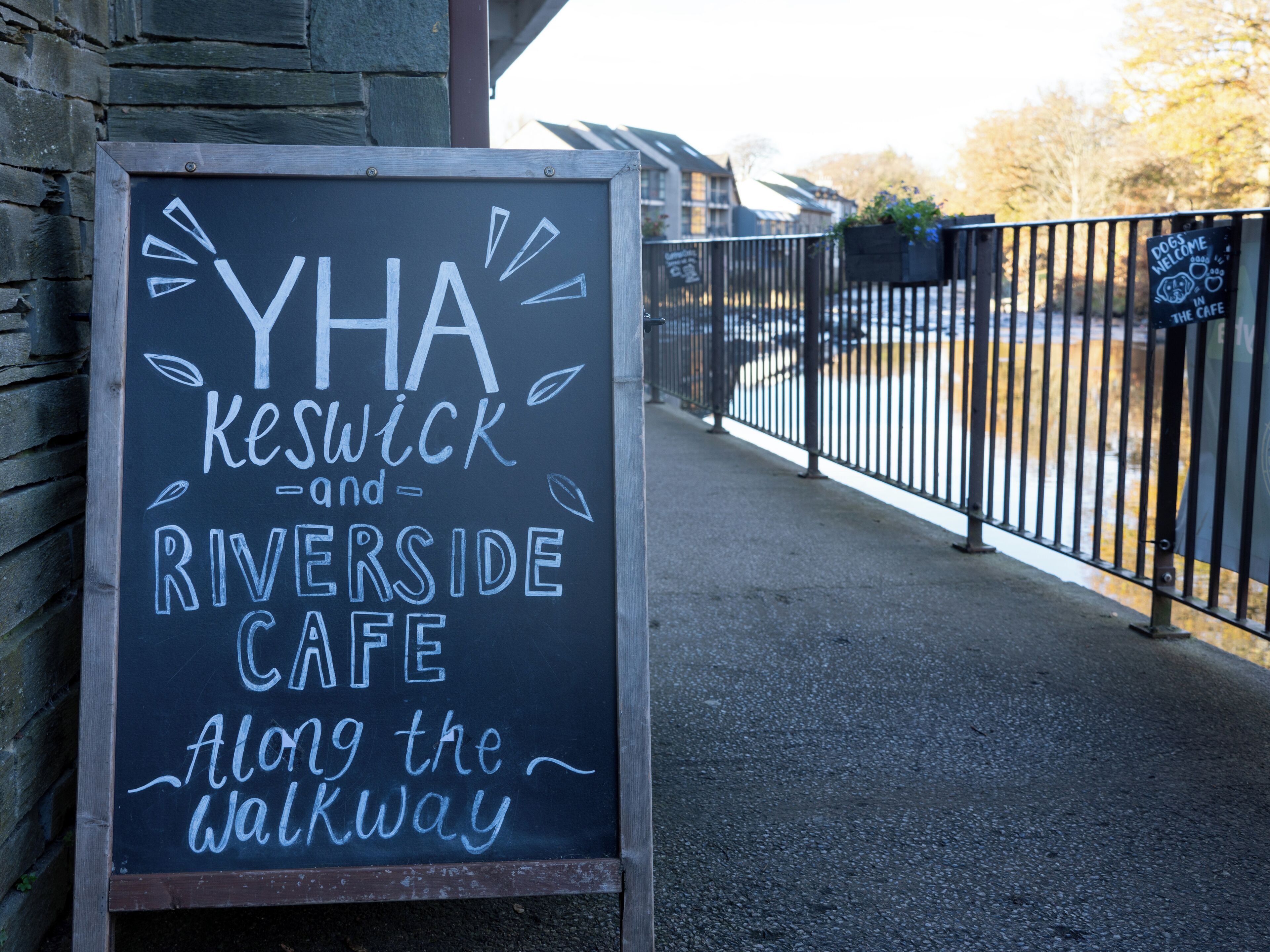 A chalkboard sign for YHA Keswick and Riverside Cafe along the walkway.