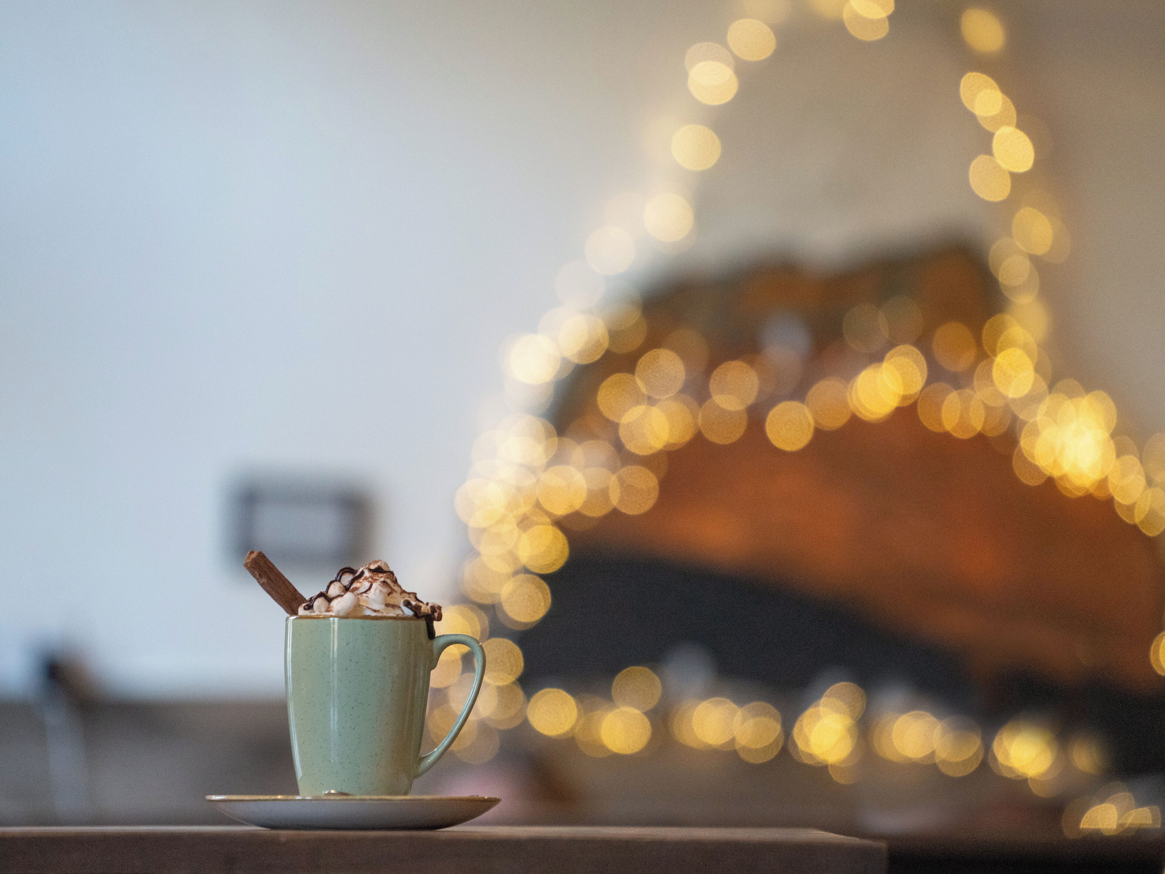 Una taza de chocolate caliente sobre un platito, con un fondo desenfocado de luces.