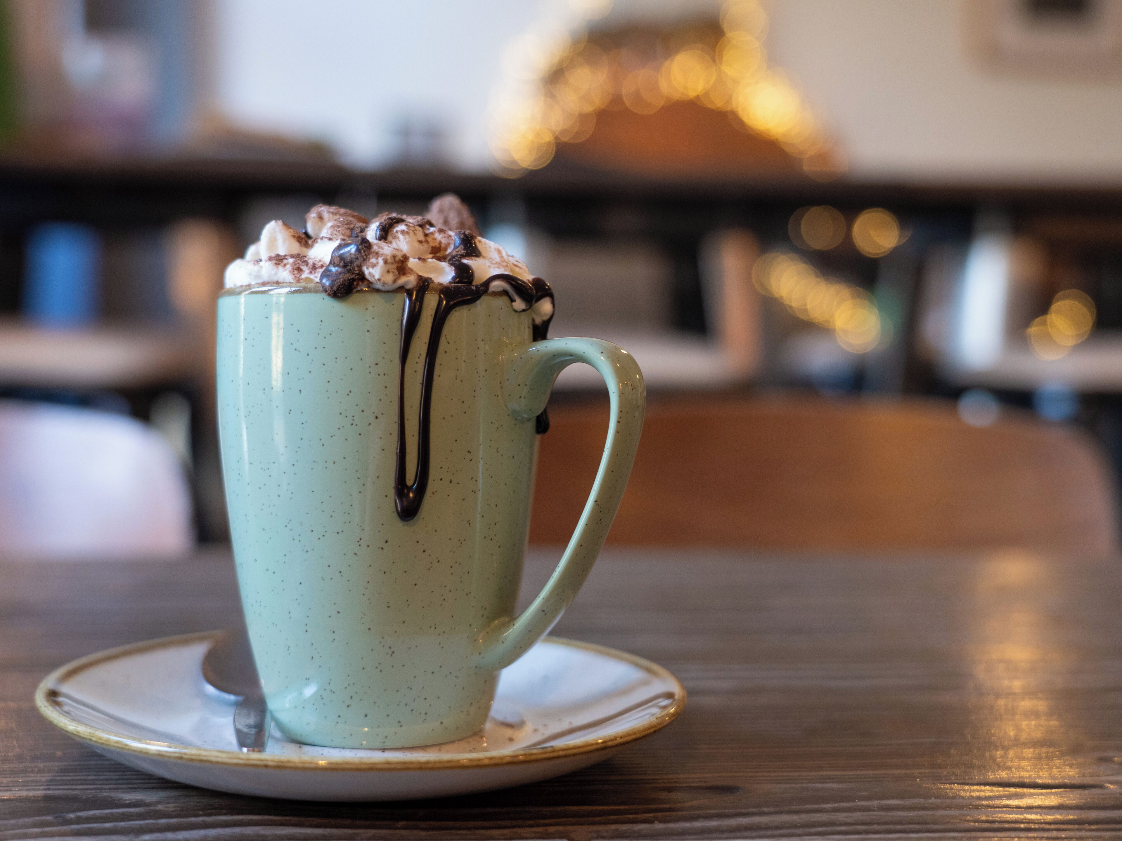 A ceramic mug with a handle, filled with a beverage and topped with whipped cream and chocolate syrup, placed on a saucer.