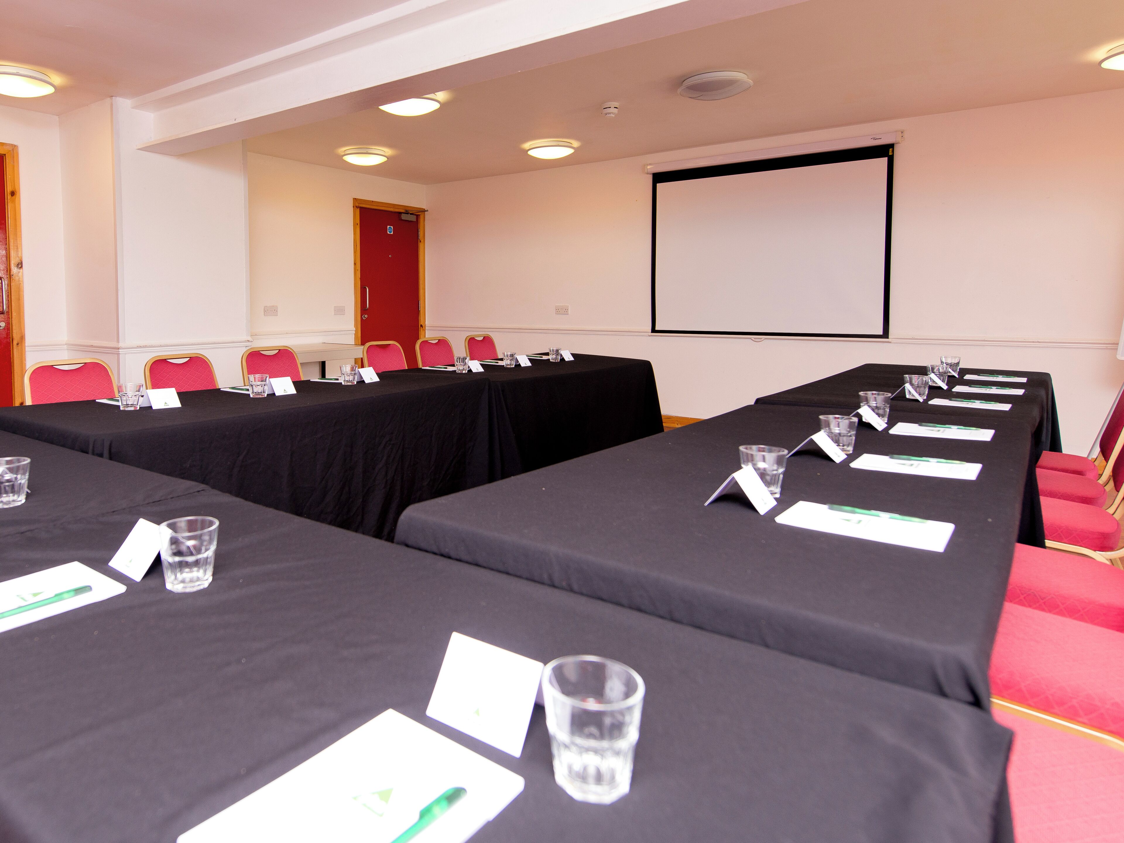 A conference room with multiple tables, chairs, and a projector screen.