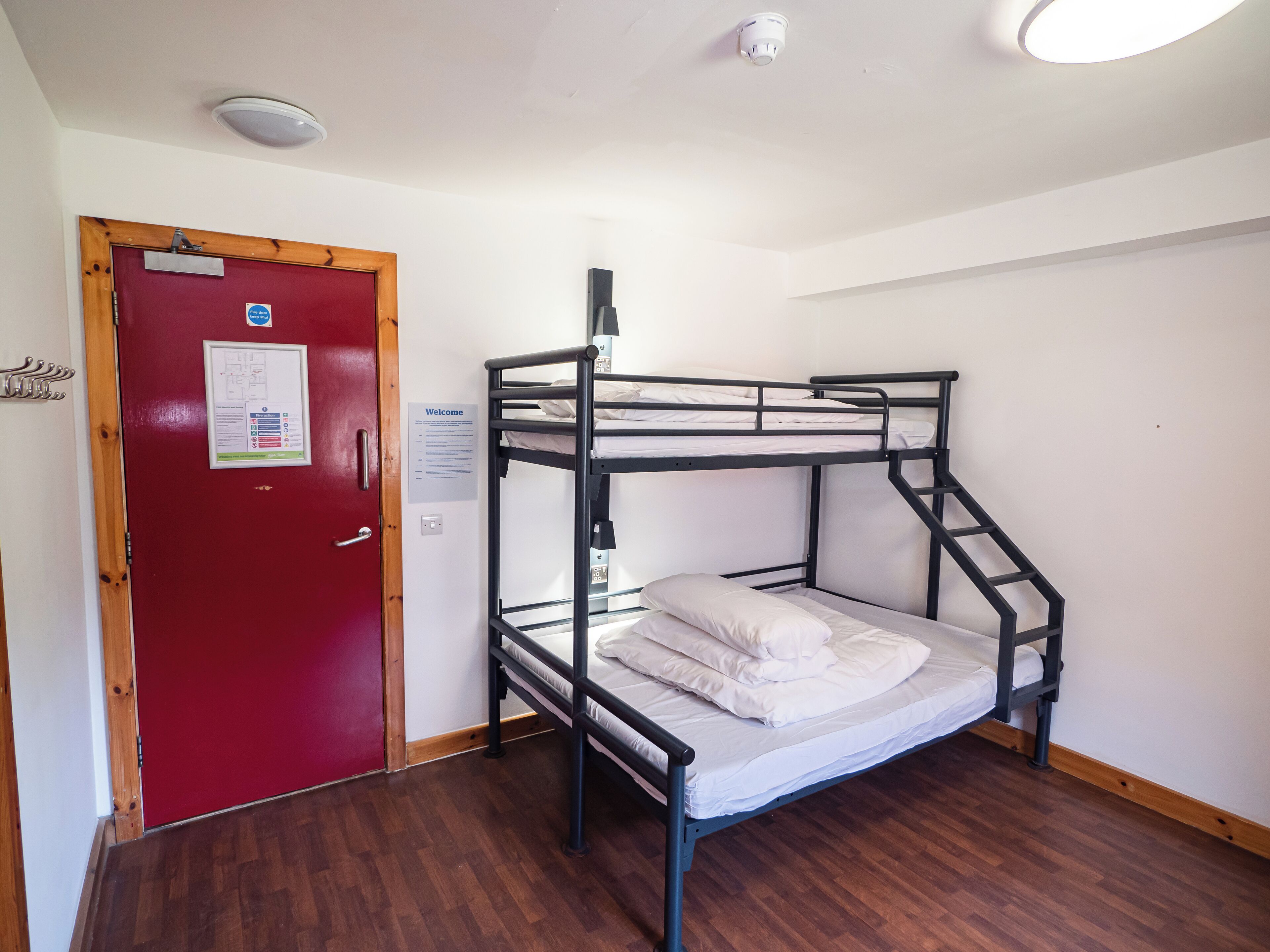 Ein Schlafraum mit Etagenbetten, einer roten Tür, einer weißen Wand und einem Holzboden.