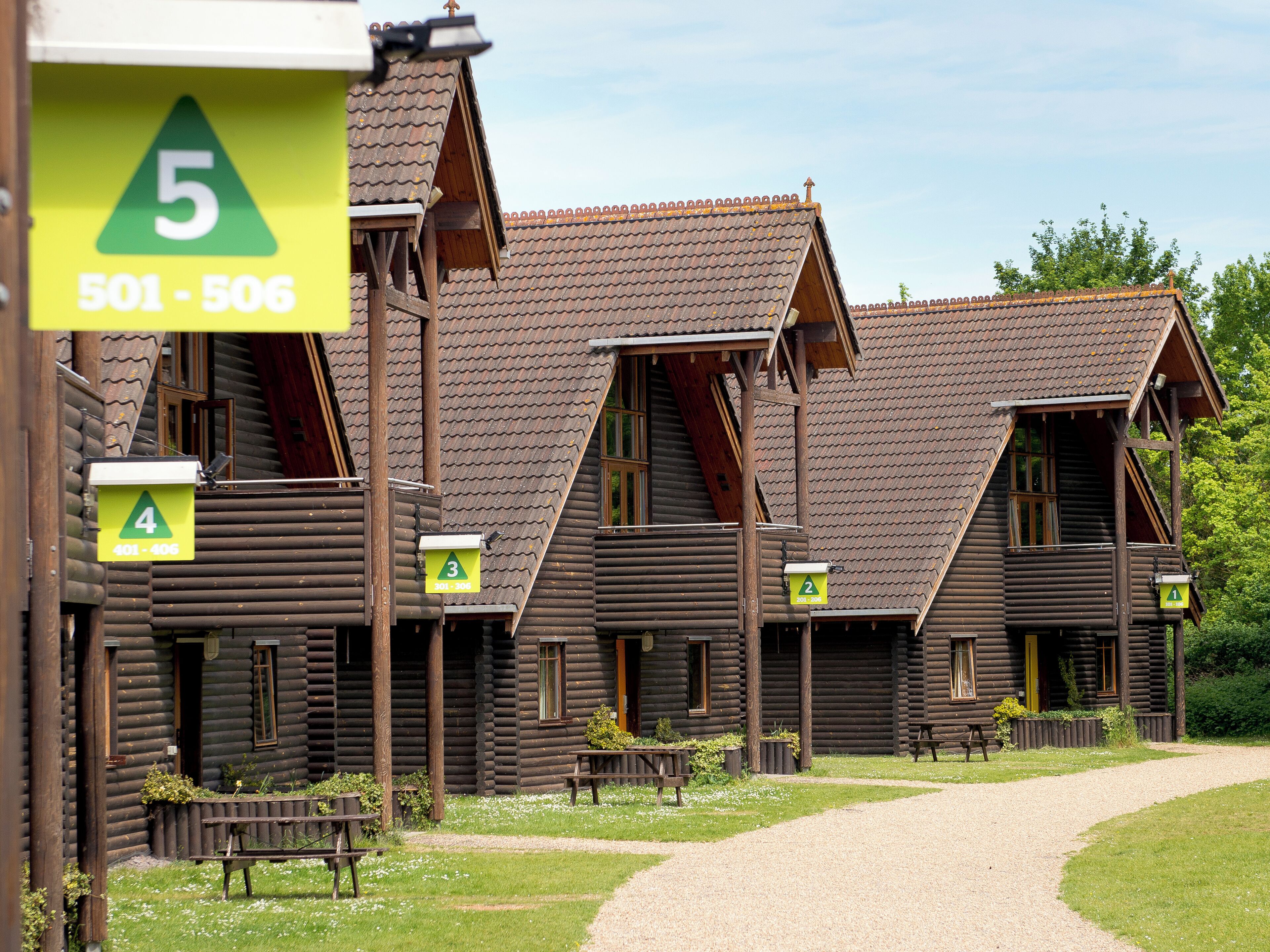 A row of log cabins with numbered signs indicating room numbers and contact numbers.