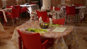 A dining area with tables covered in floral tablecloths, red chairs, and a basket of lemons on one table. - Pemicsa Hotel (Accra)