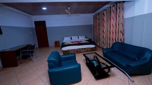 A room with a bed, a blue sofa, a desk, and a coffee table. - Pemicsa Hotel (Accra)